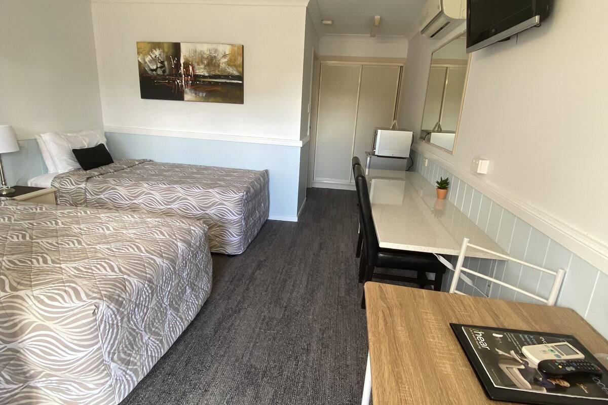 A hotel room with two beds, a desk, a chair, a TV, and a painting on the wall.