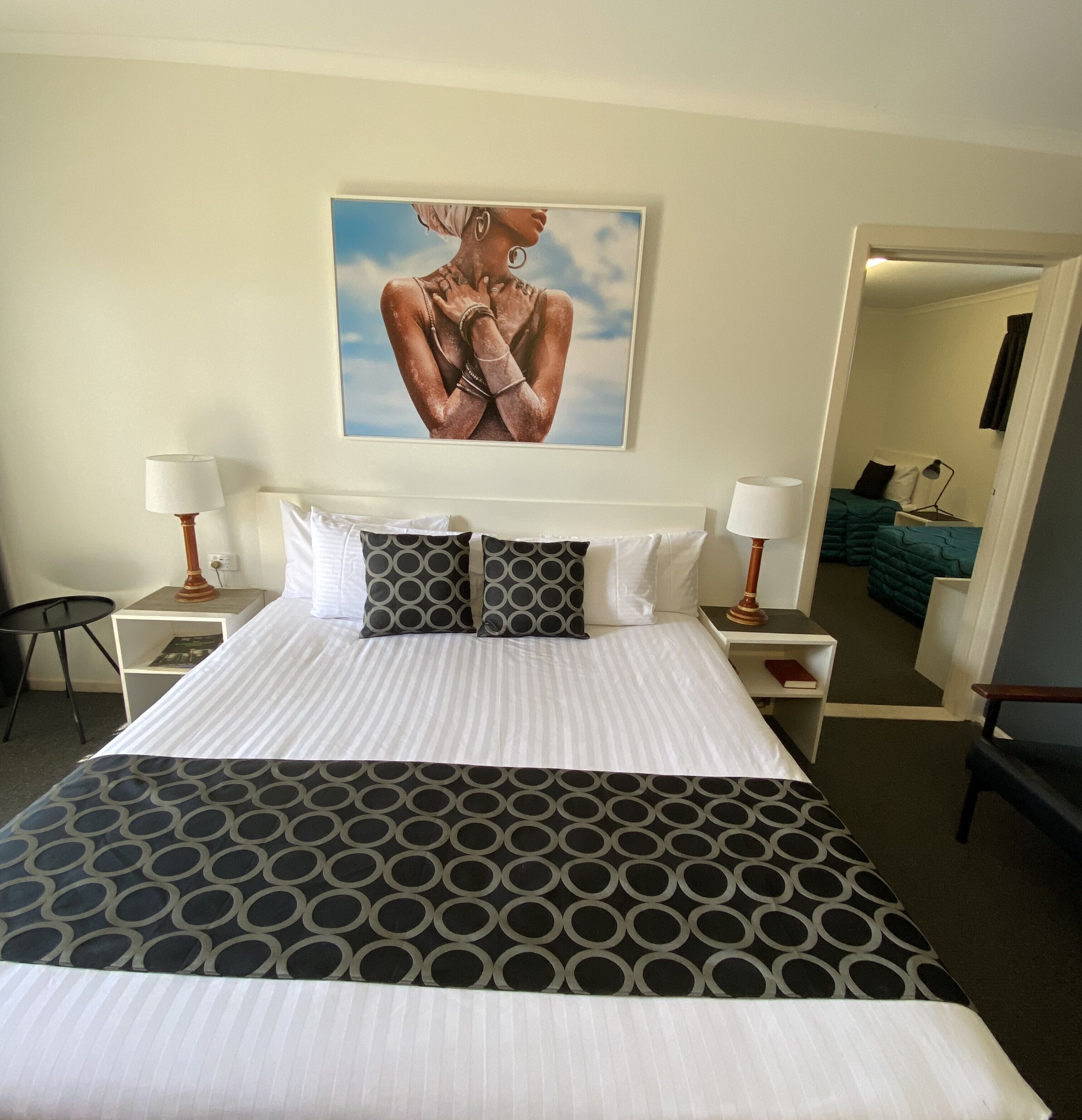 Een hotelkamer met een groot bed, twee nachtkastjes, een stoel en een schilderij aan de muur.