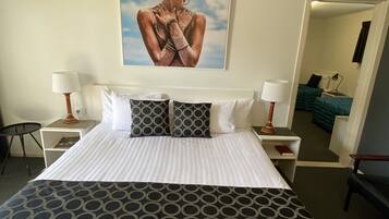 Een hotelkamer met een groot bed, twee nachtkastjes, een stoel en een schilderij aan de muur.