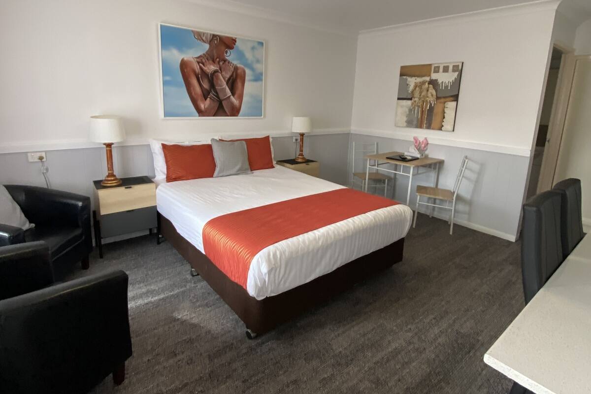 A hotel room with a large bed, two bedside tables with lamps, a desk with a chair, and a painting on the wall.