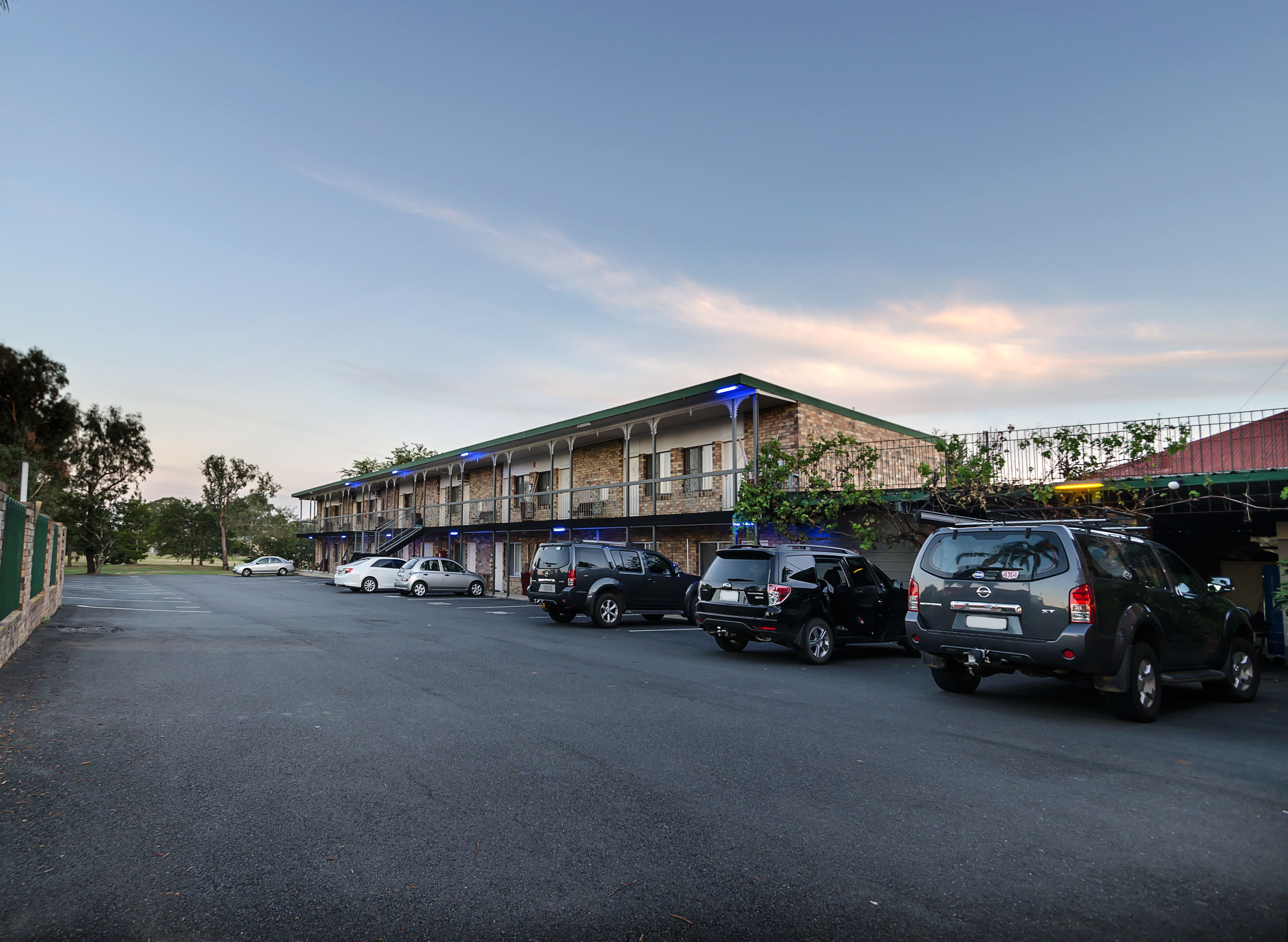 A parking lot with several cars, a building with multiple floors and balconies, and a clear sky.