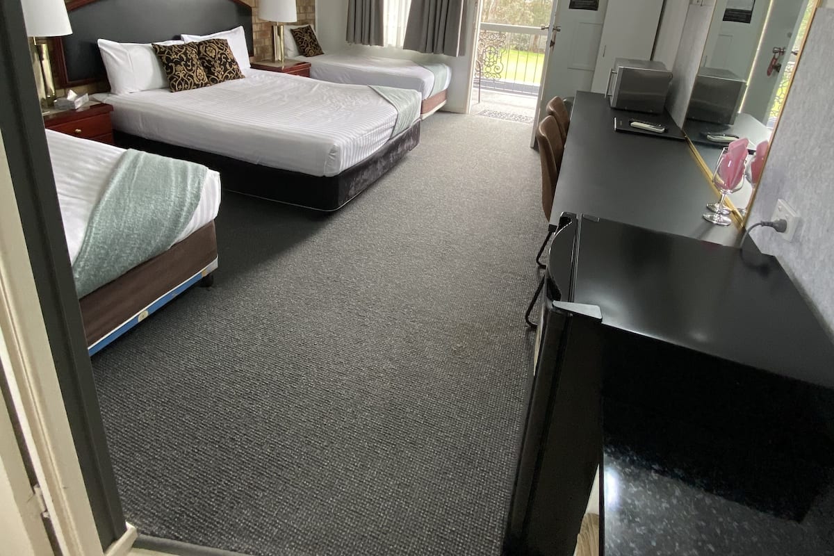 A hotel room with two beds, a desk, a mirror, and a view of the outdoors.