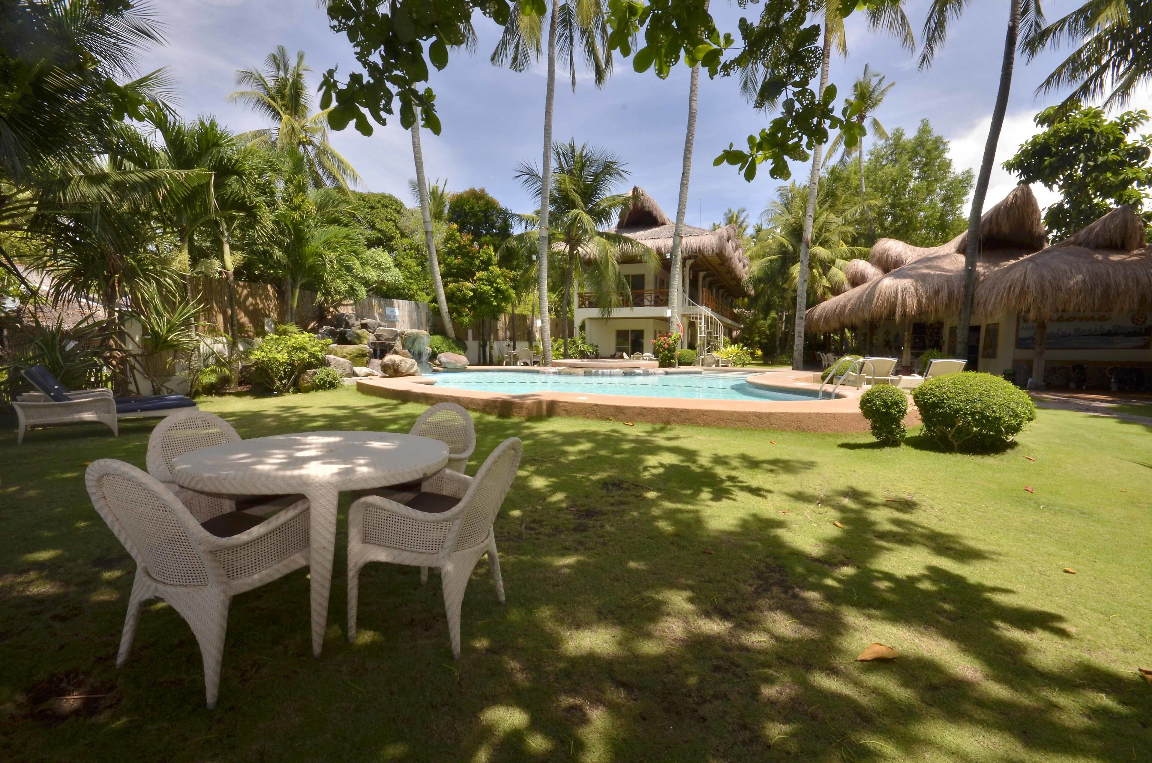 A pool area with a thatched-roof building, surrounded by palm trees and a well-maintained lawn.