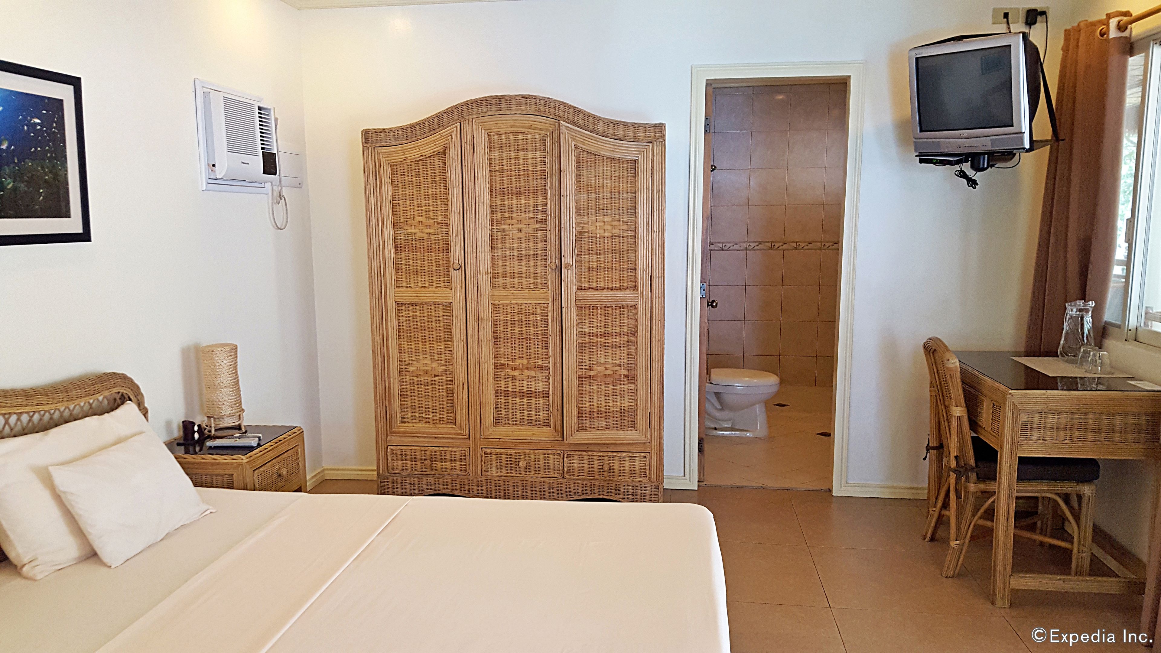 Une chambre comprenant un lit, une armoire, un bureau avec une chaise, une télévision et une salle de bain avec des toilettes.