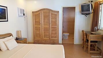 Une chambre comprenant un lit, une armoire, un bureau avec une chaise, une télévision et une salle de bain avec des toilettes.