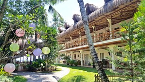 Un resort con una edificación de techo de paja, un espacio al aire libre cubierto y un jardín cuidado.