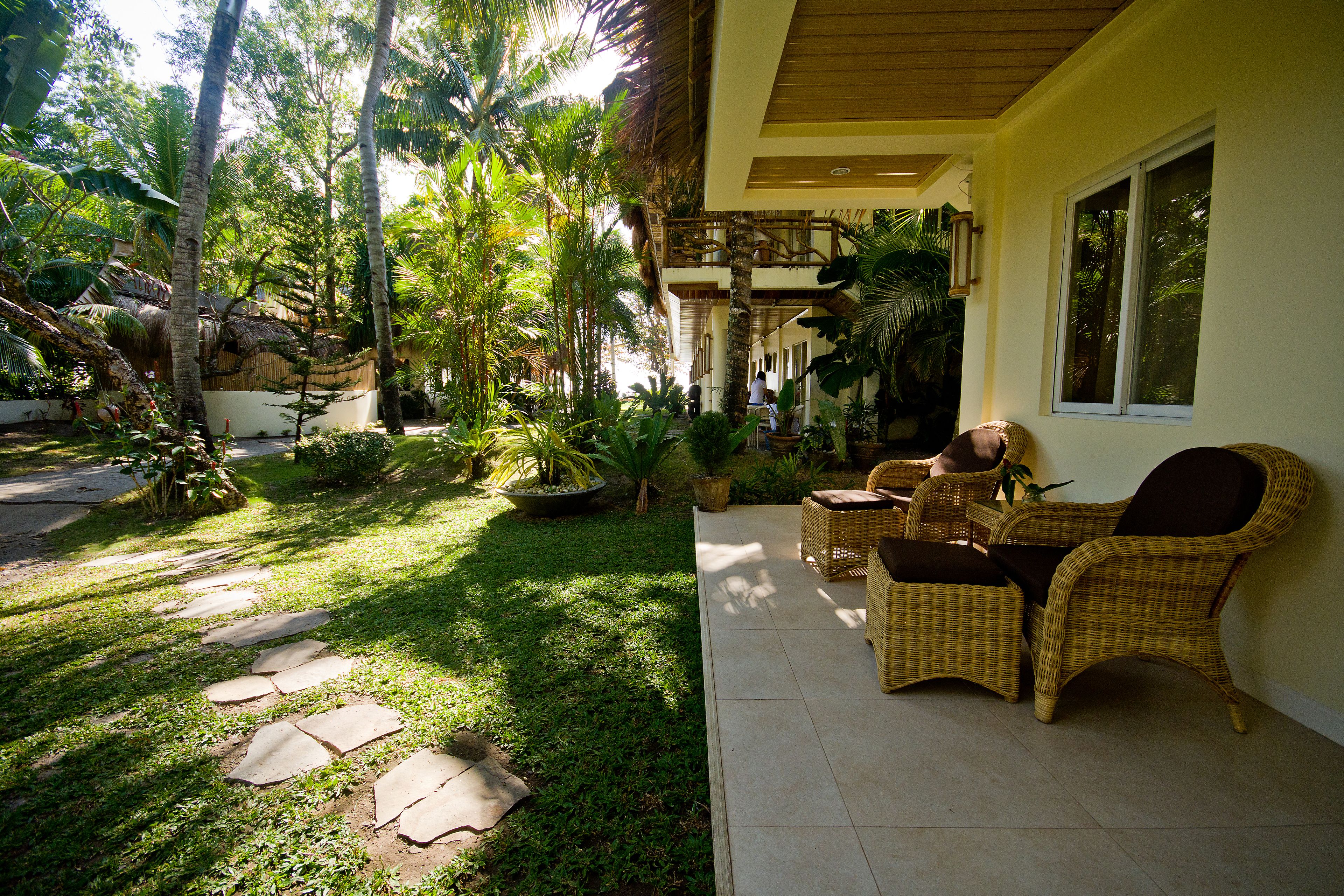 Un espace patio aménagé avec des meubles en osier, une structure à toit de chaume et une vue sur le jardin environnant.
