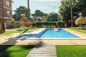 Una piscina al aire libre, sombrillas, sillones reclinables de piscina