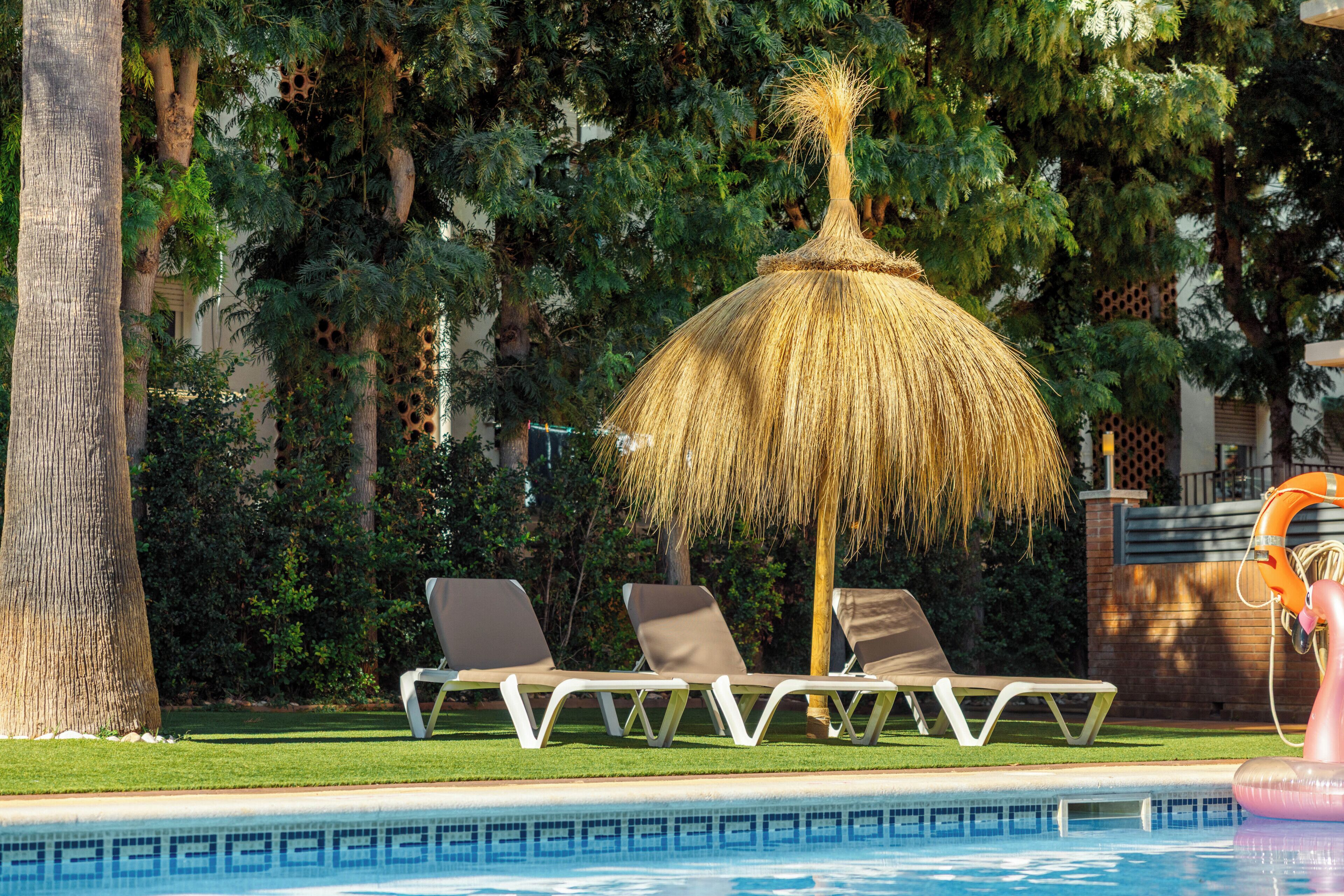 Una piscina al aire libre, sombrillas, sillones reclinables de piscina
