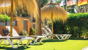 A garden area with lounge chairs, a thatched umbrella, and flags.