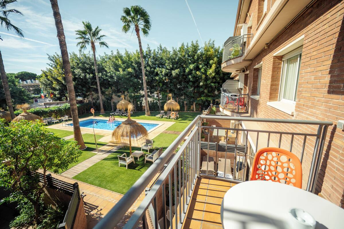 A balcony with a view of a swimming pool, palm trees, and a brick building.