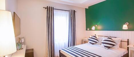 A bedroom with a bed, curtains, a bedside table, a lamp, and a green accent wall.