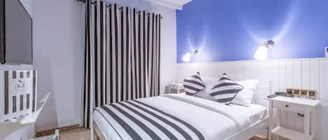 Un dormitorio con una cama, una mesita de noche, una lámpara, una ventana con cortinas y una repisa en la pared.
