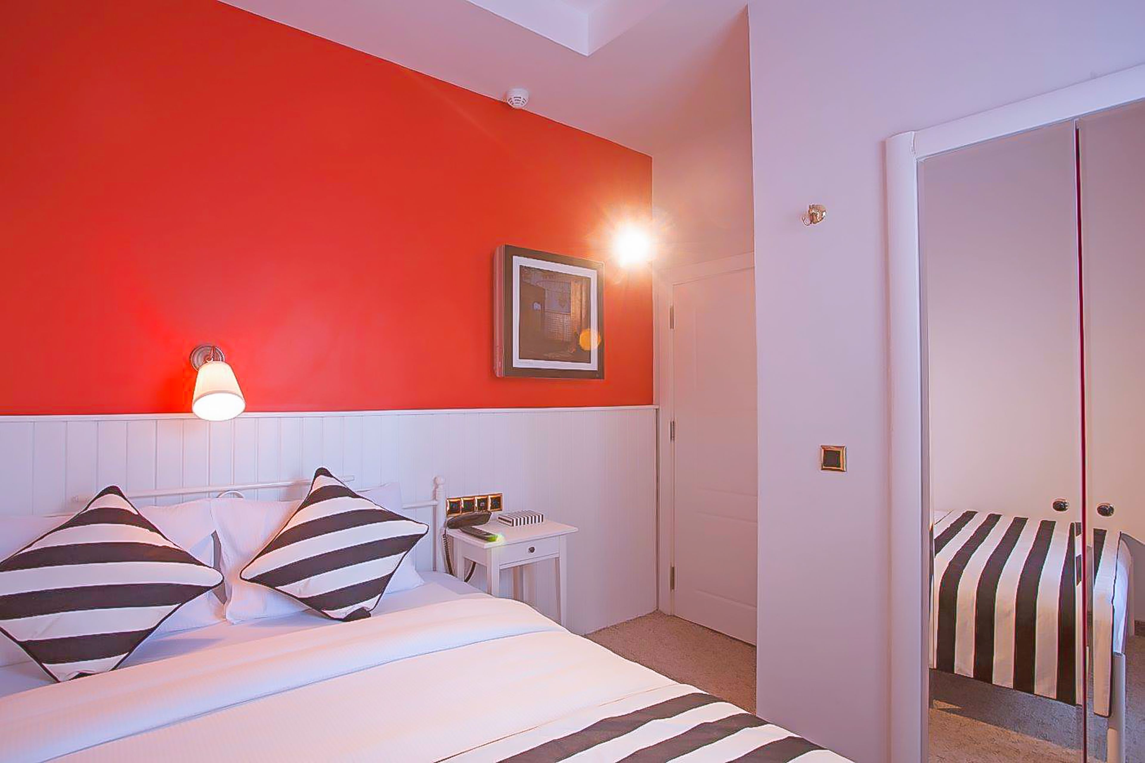 A hotel room with a bed, a bedside table, a lamp, a framed picture, and a wardrobe.