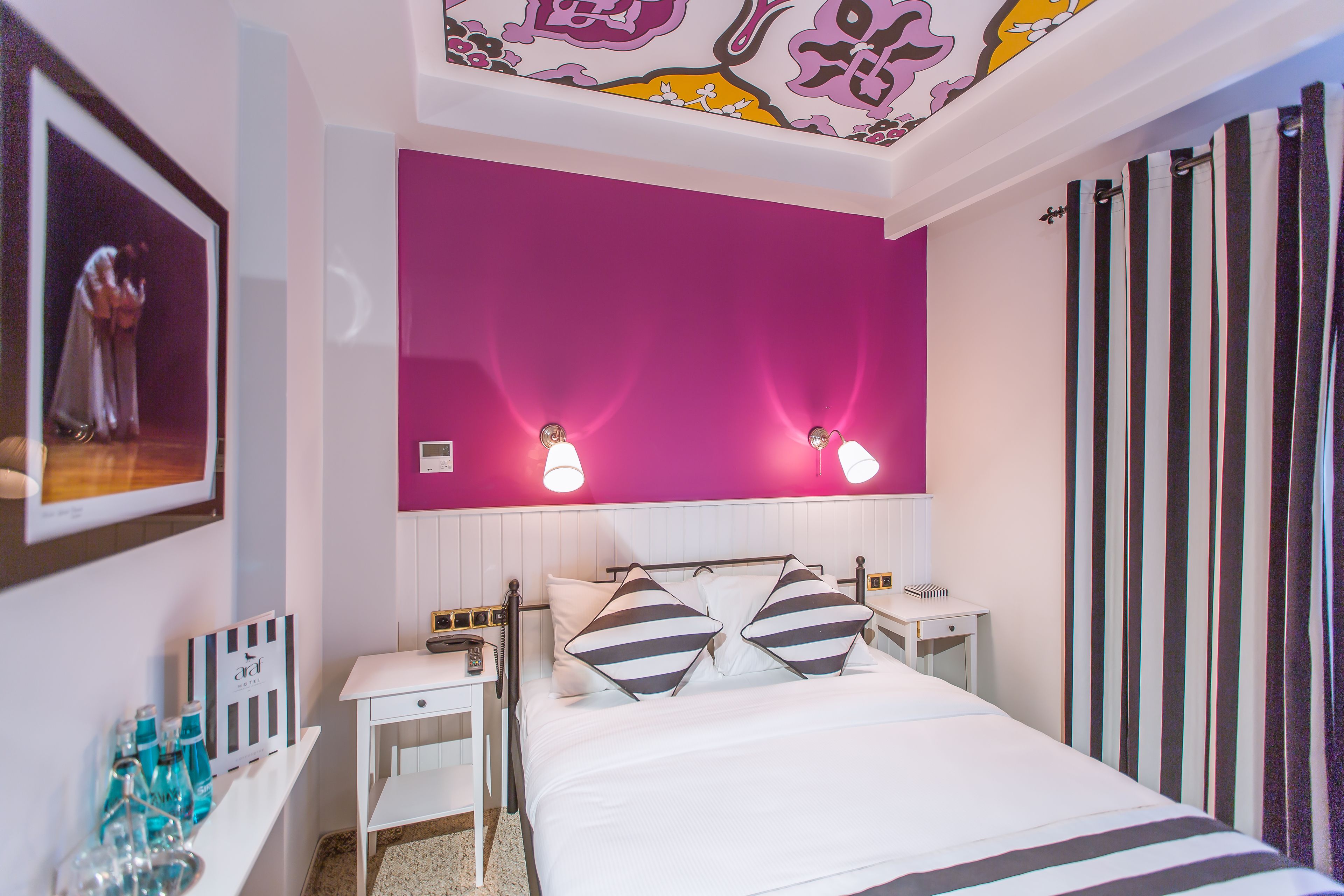 Ein Hotelzimmer mit Bett, Nachttischen, einem Spiegel und einer Wand mit einem Bilderrahmen.