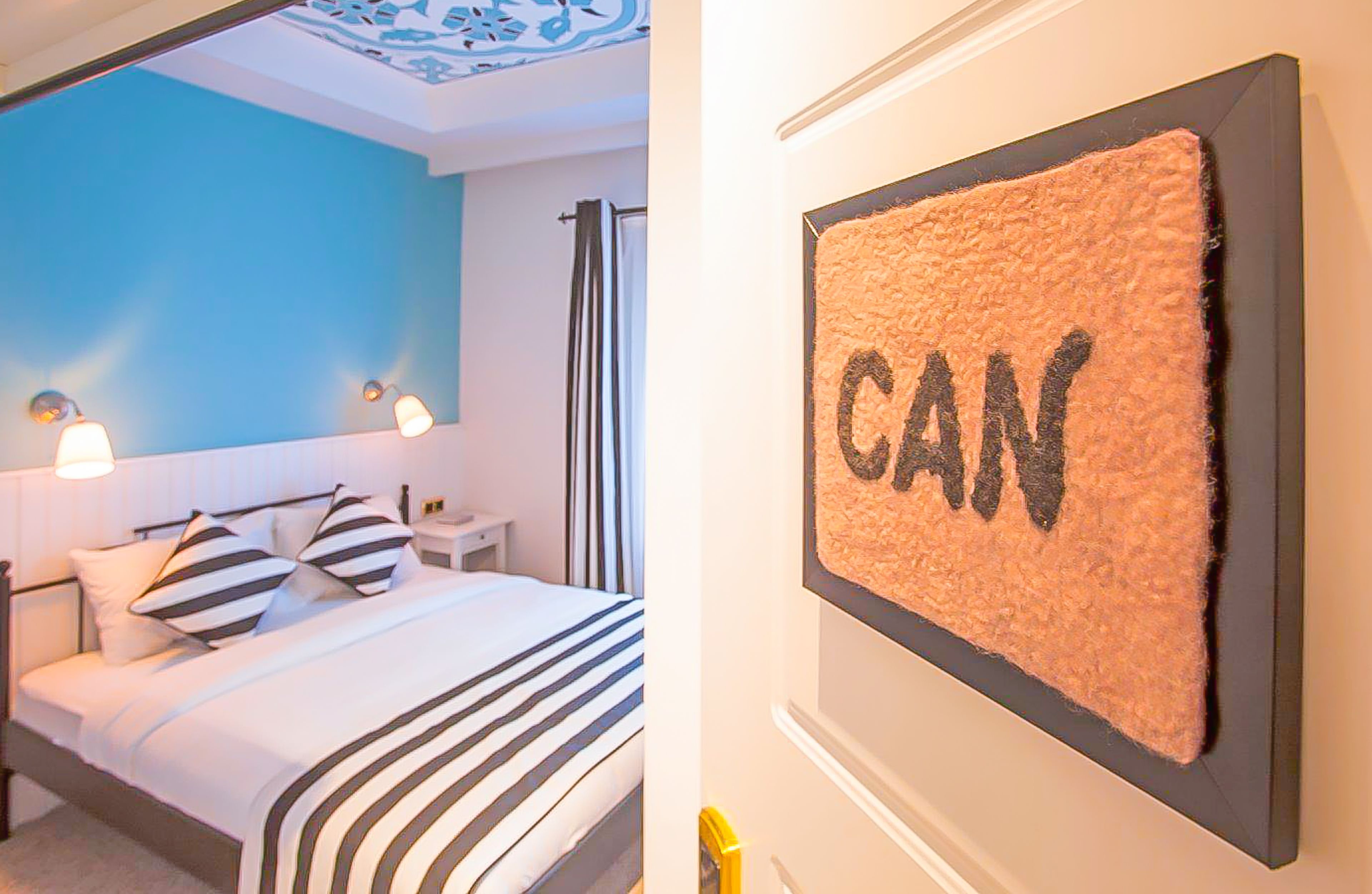 A hotel room with a bed, bedside lamps, and a wall-mounted sign with the word "CAN".