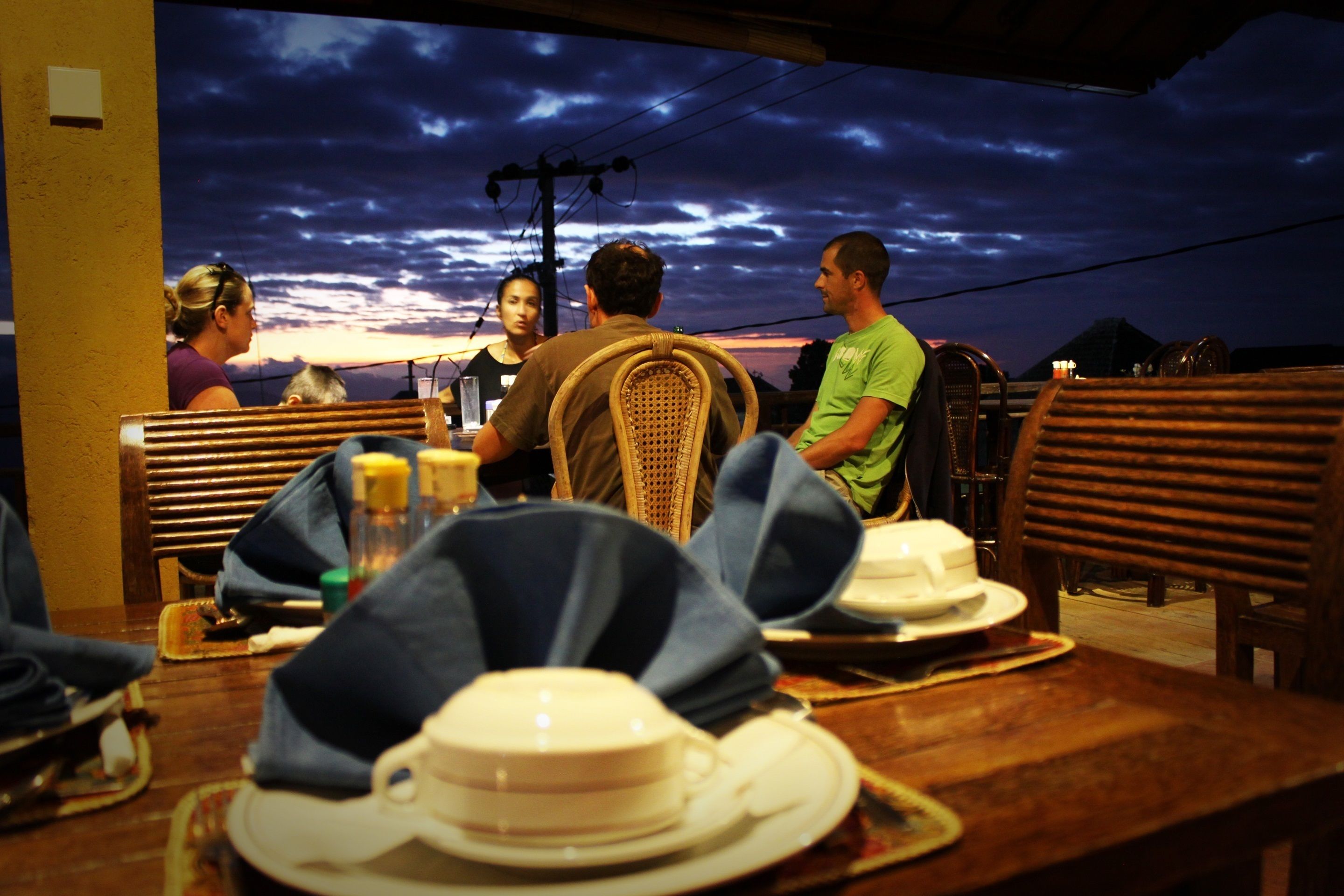 Un restaurant avec des tables et des chaises en bois, une vue sur le coucher de soleil et une ambiance décontractée.