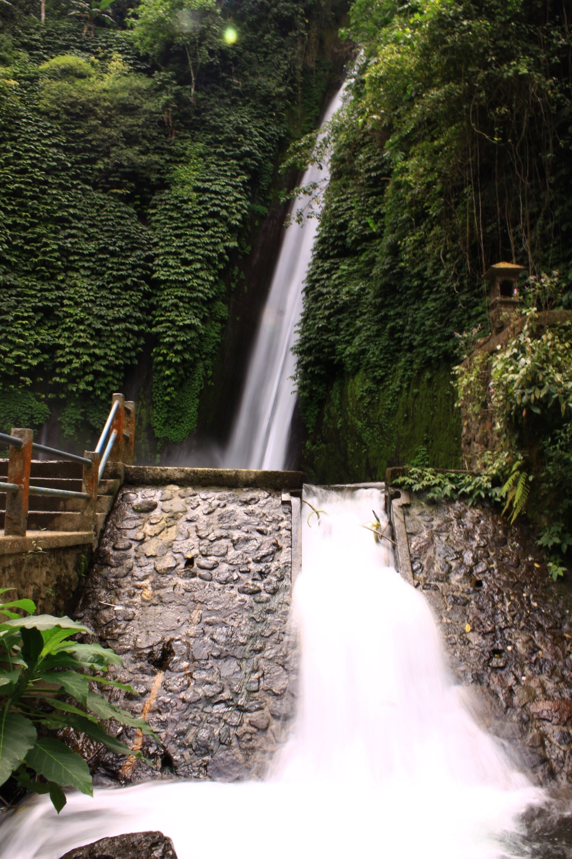 A waterfall cascading down a rocky ledge surrounded by dense greenery.