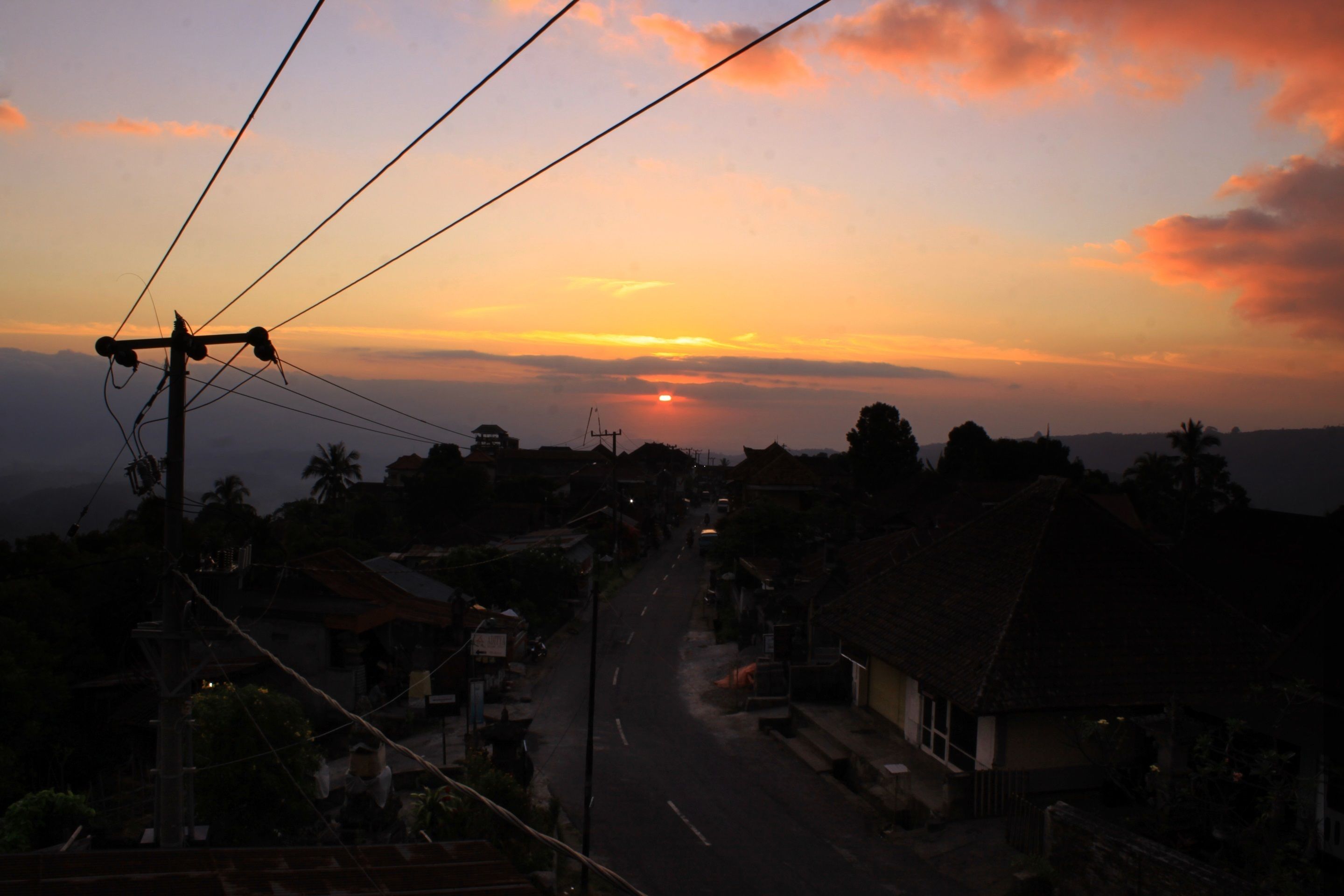 A street view at sunset with houses and power lines.