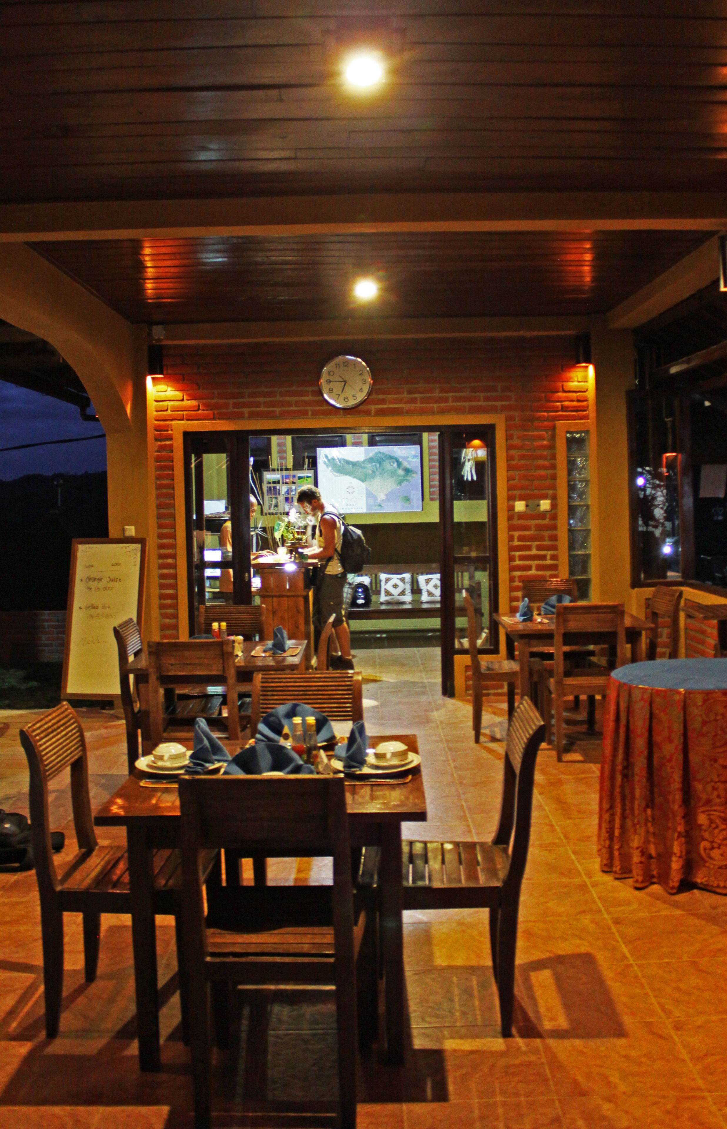 Un restaurant en plein air avec des tables et des chaises en bois, une horloge au mur et un panneau affichant le menu.