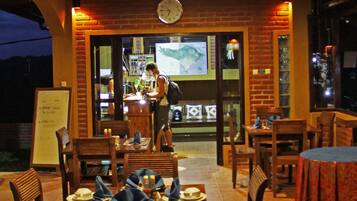 An outdoor restaurant with wooden tables and chairs, a clock on the wall, and a menu board.