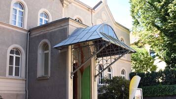 Ein Gebäude mit einer grünen Tür, einer Überdachung und einer Bank vor der Fassade.