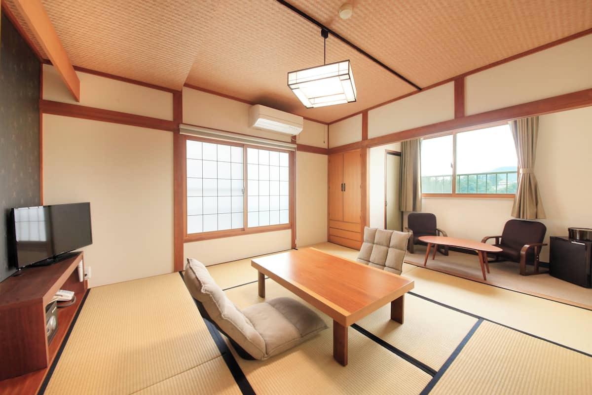 Una habitación japonesa tradicional con suelo de tatami, una mesa de madera baja, un sofá y un televisor sobre un soporte de madera.