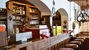 Uma área de bar com prateleiras de madeira repletas de garrafas e copos, uma decoração de veado aveludado e uma fileira de banquetas de madeira.