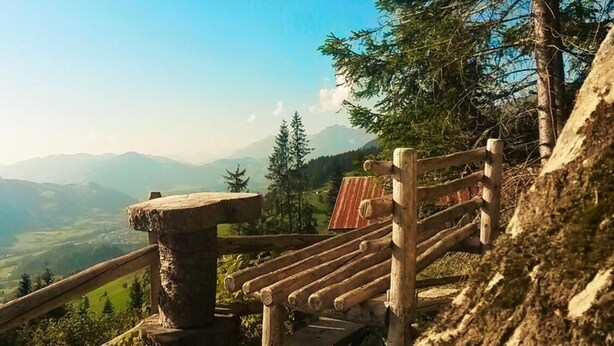 Um banco de madeira com guarda-corrimão de metal com vista para uma paisagem montanhosa.