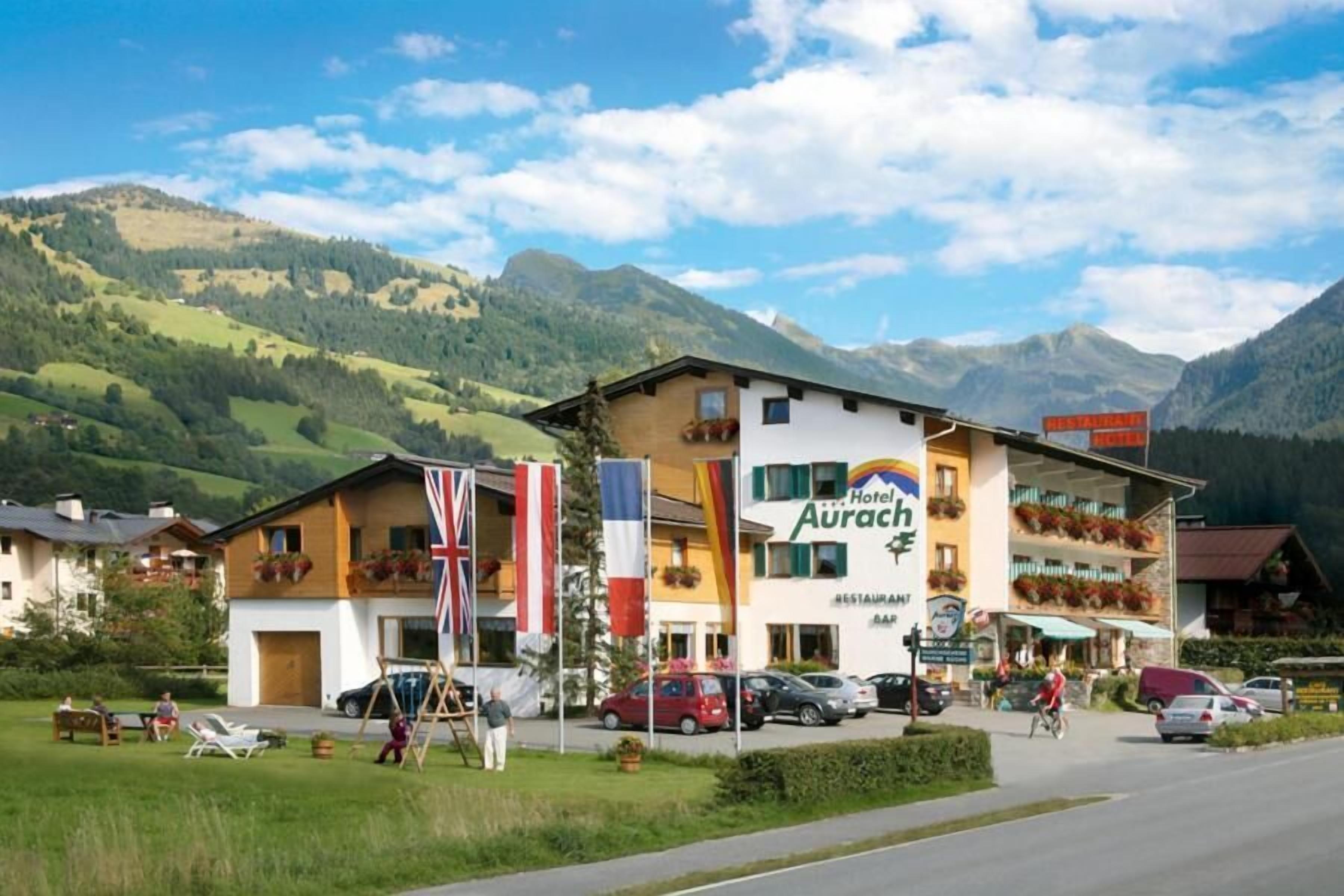 Hotel con montañas al fondo, que cuenta con un restaurante y bar en la planta baja, y banderas del Reino Unido, Francia y Alemania.