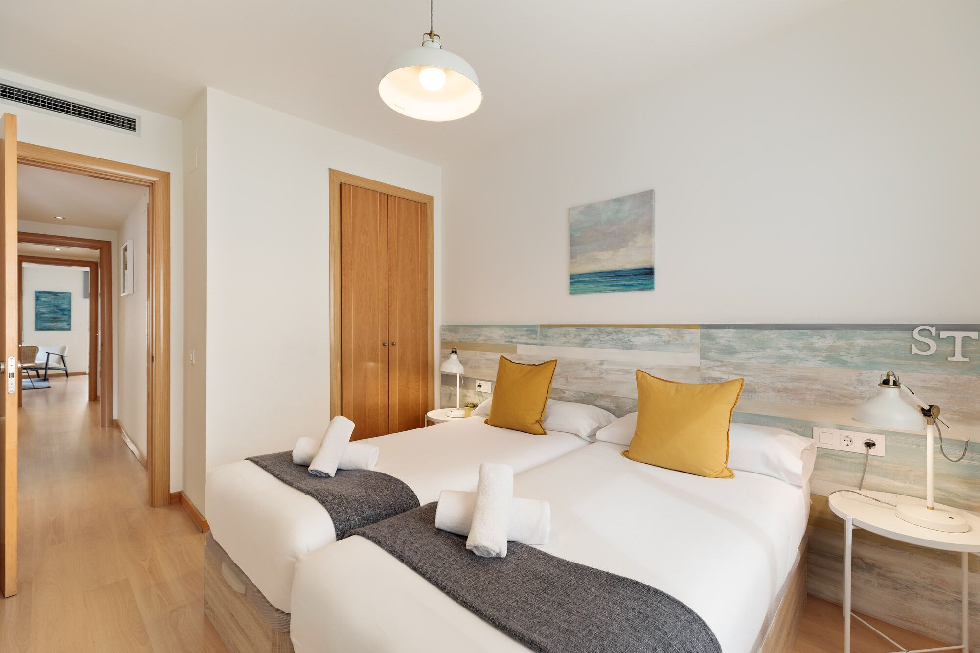 A hotel room with a large bed, a wooden wardrobe, a painting of the sea, and a view of the sea through the window.