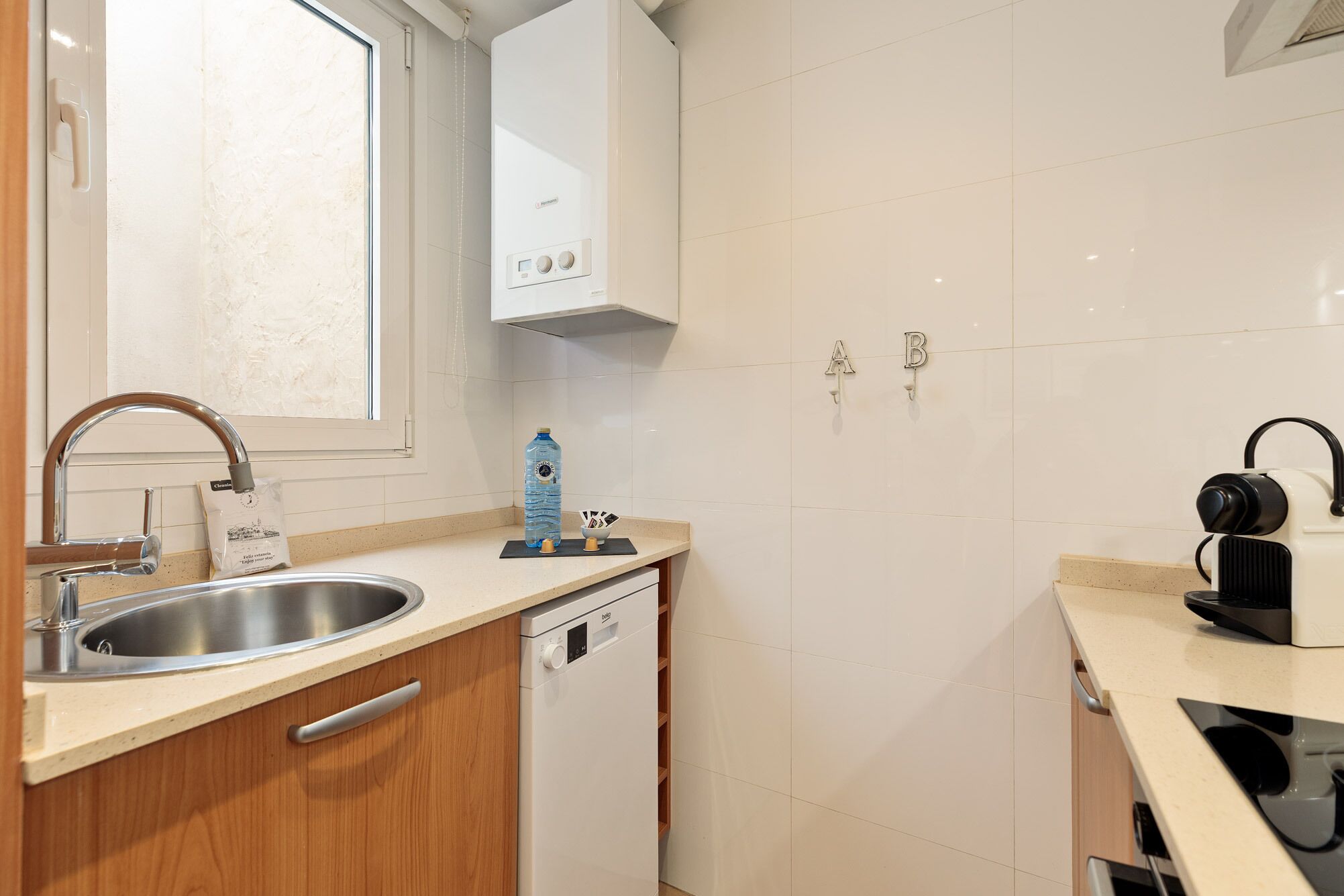 Una cocina compacta con un lavamanos de acero inoxidable, lavavajillas y cafetera.