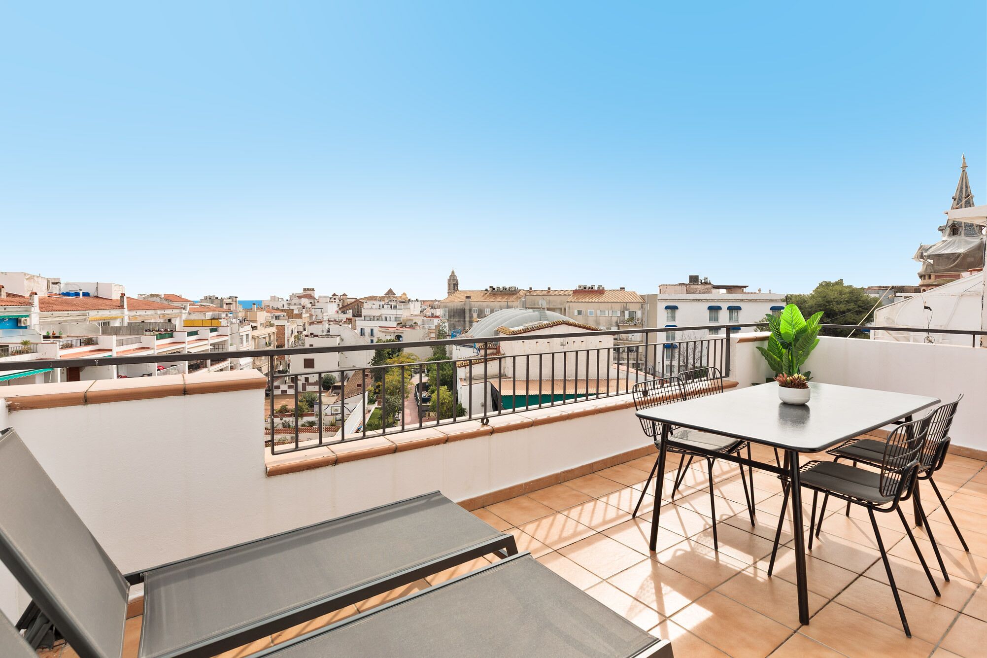 Ein Balkon mit Tisch und Stühlen, einem Blumentopf und Blick auf die Stadt.