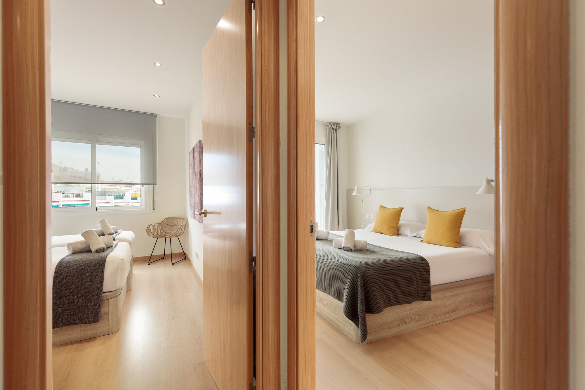 Una habitación de hotel moderna con una cama, una silla, un escritorio y vistas a la ciudad a través de amplios ventanales.