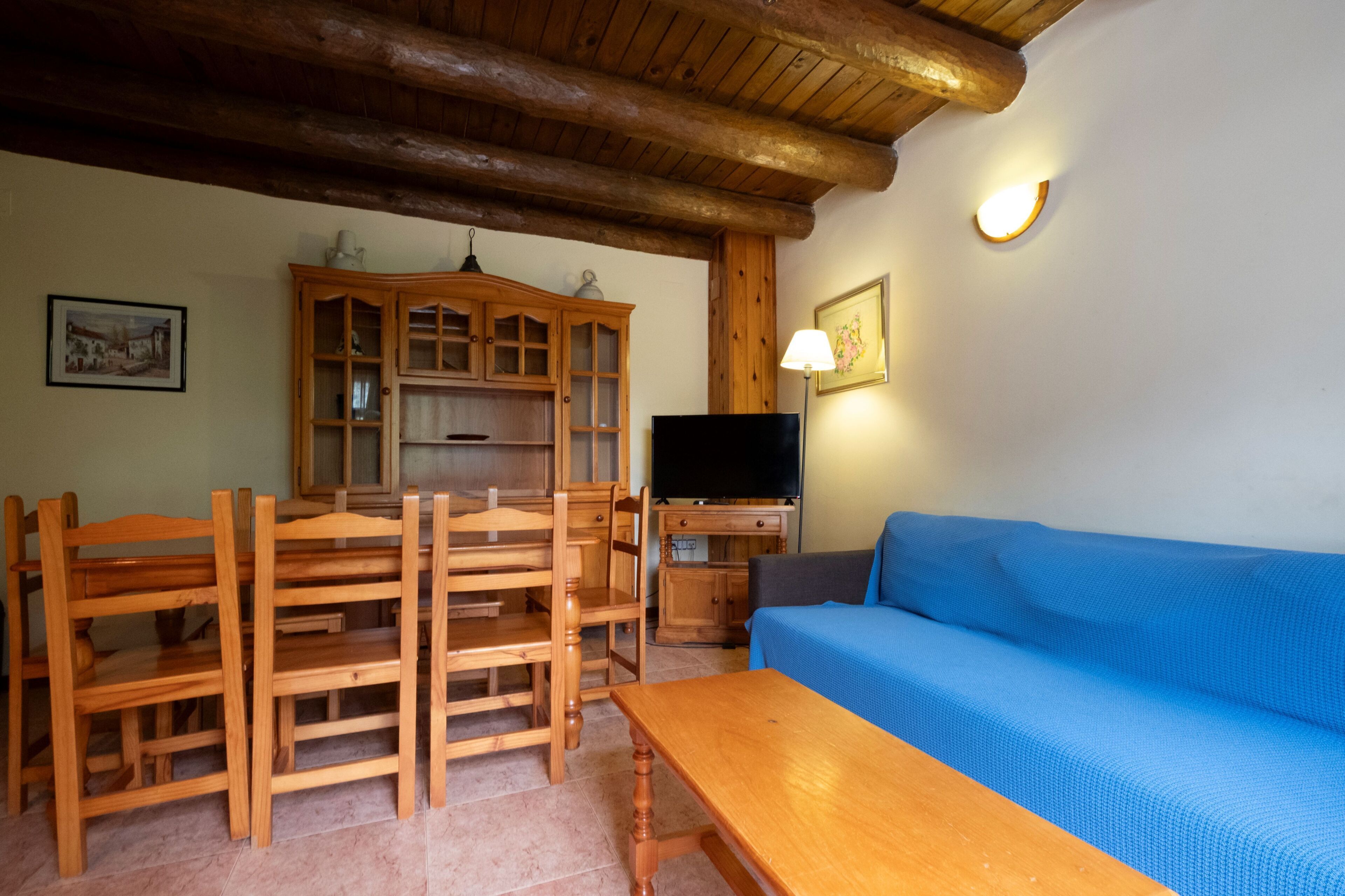 A wooden dining table with chairs, a blue sofa, a television, and wooden cabinets in a room with a wooden ceiling.