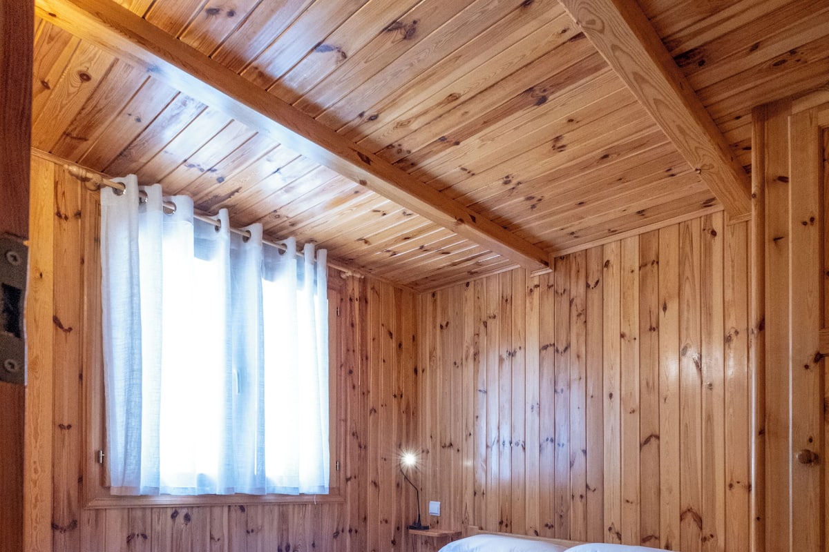Una habitación con paneles de madera, una cama, cortinas y un ventanal.
