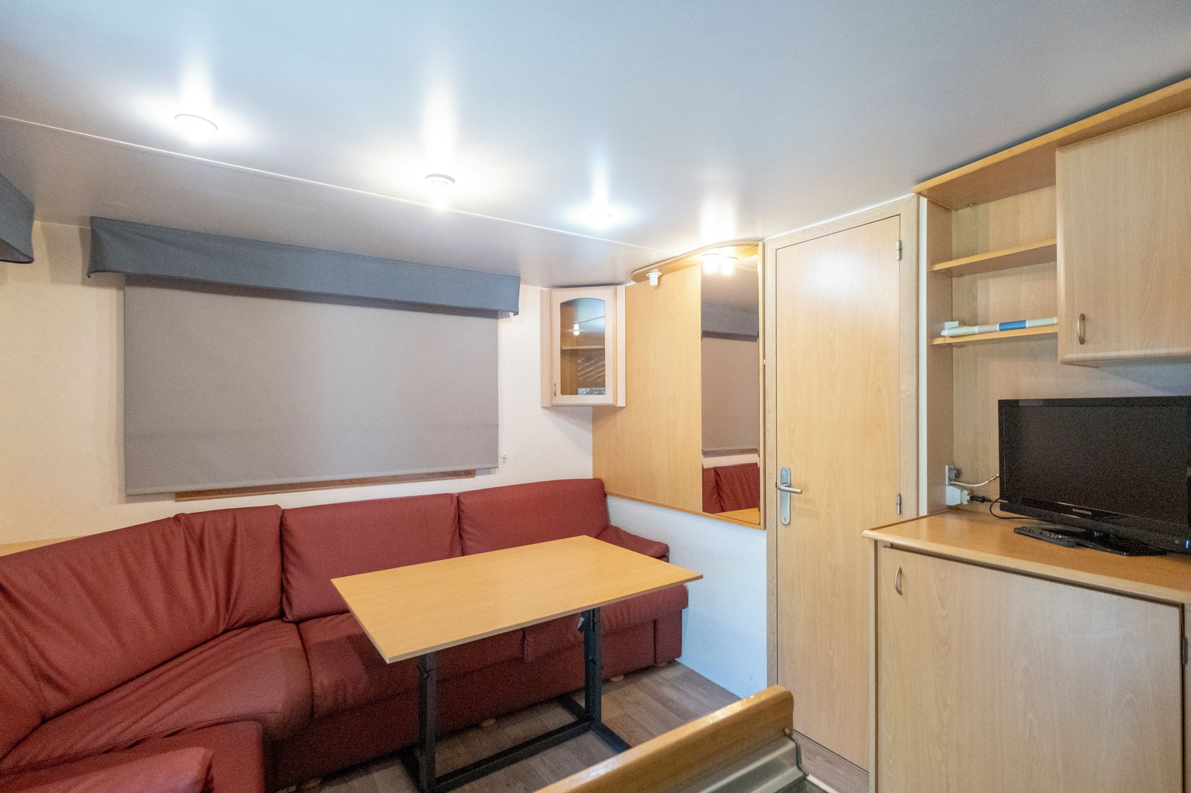 Una habitación compacta con sofá rojo, una mesita de madera, televisión y un armario.