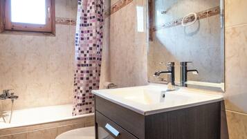 A bathroom with a bathtub, toilet, vanity with drawers, and a large mirror.