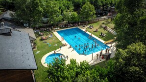 Ein großer rechteckiger Pool, umgeben von einer Liegefläche, mit einer Rasenfläche und Bäumen im Hintergrund.