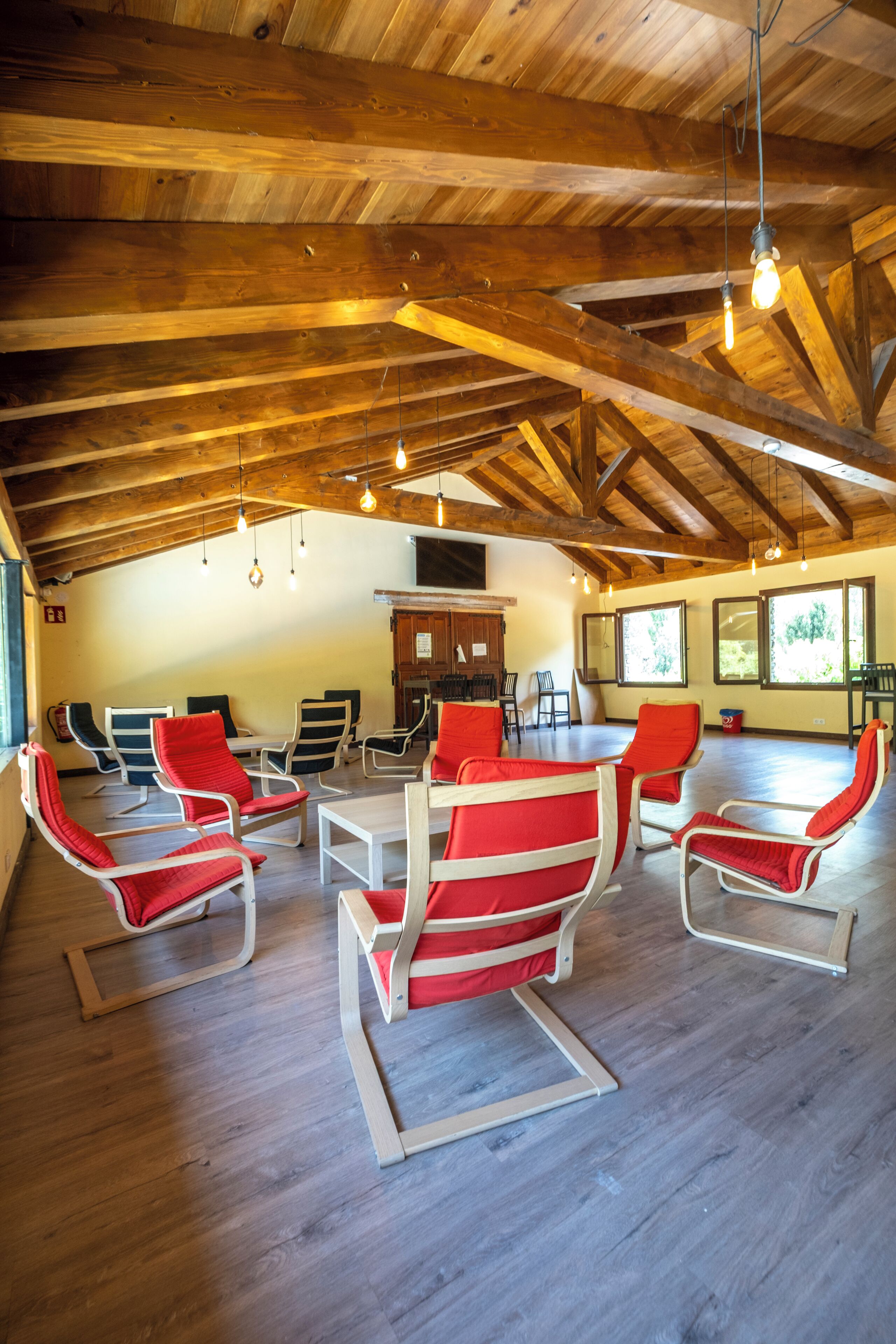 A spacious room with wooden beams, a dining table, and red chairs.
