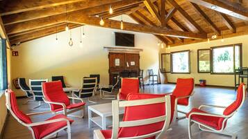 A spacious room with wooden beams, a dining table, and red chairs.
