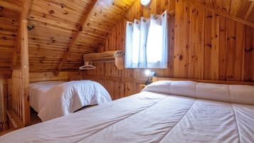 A cabin with wooden walls and a sloped ceiling, featuring two beds with white bedding and a window with curtains.