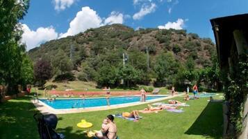 Relax by the serene pool surrounded by lush greenery and a hill, with lounge chairs and a shaded gazebo nearby.