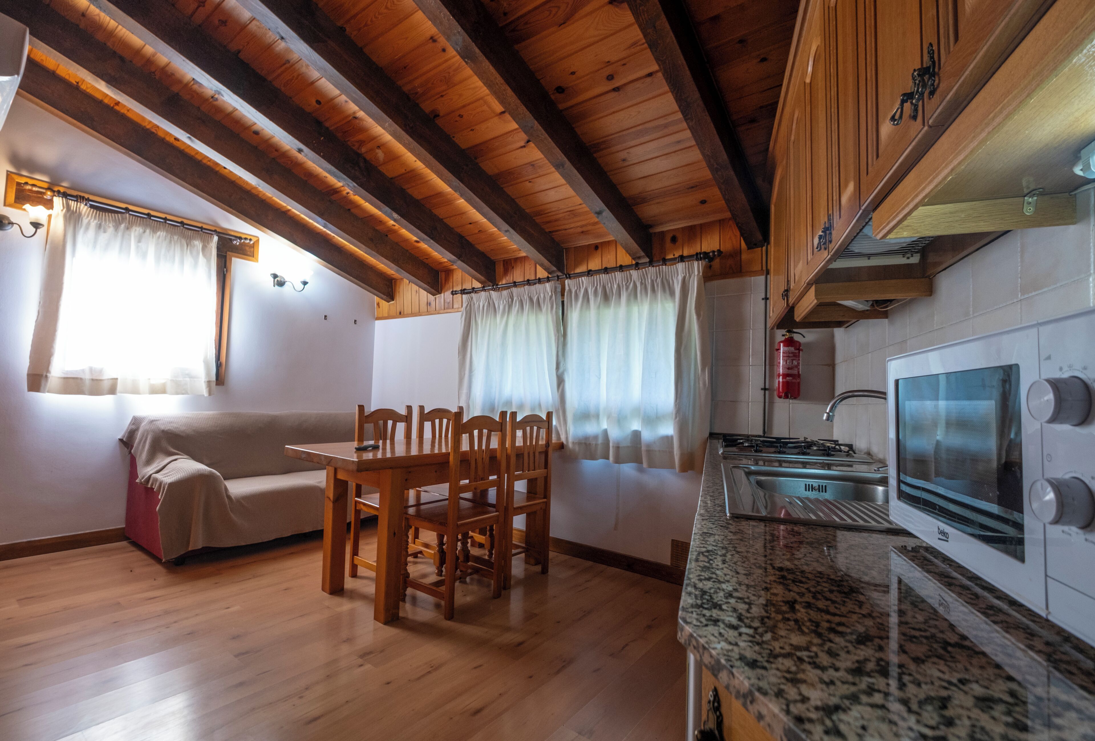 A cozy kitchen with wooden beams, a dining area with a table and chairs, and a kitchenette with a stove and microwave.