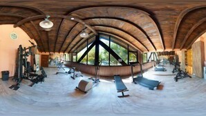 Ein Fitnessraum mit Holzbalken, Trainingsgeräten und großen Fenstern.