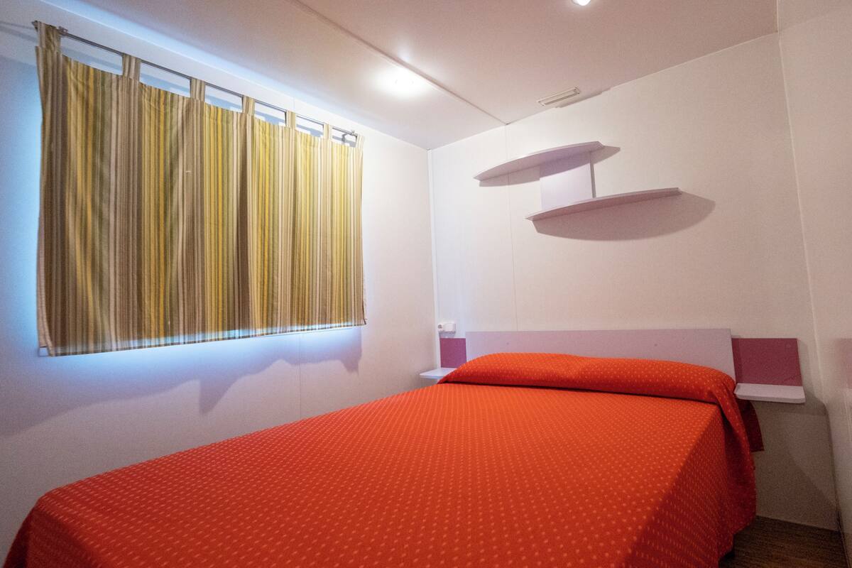 Una habitación con una cama, una ventana con cortinas, una estantería y una lámpara en el techo.