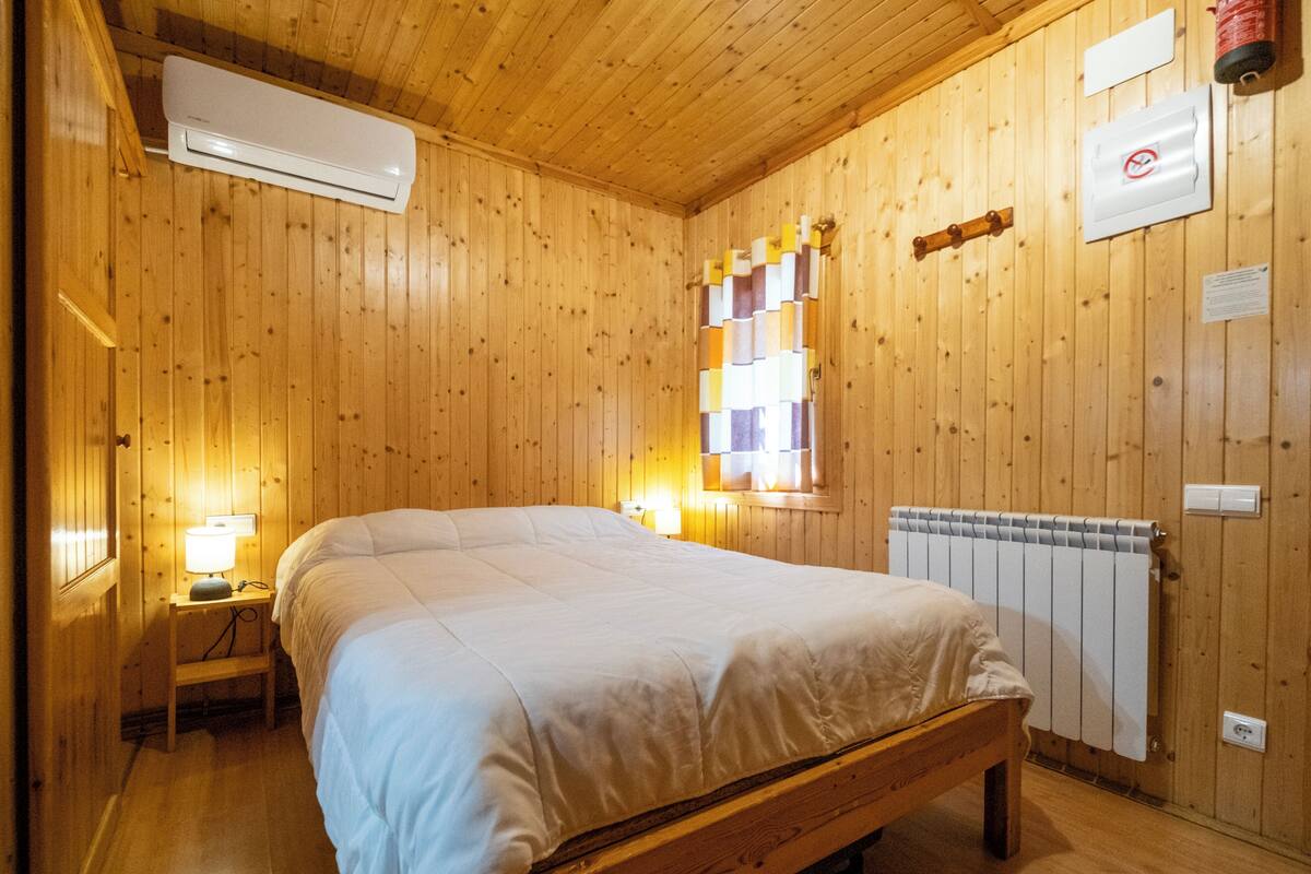 Una habitación con paneles de madera, una cama, lámparas de noche, un radiador y un aire acondicionado de pared.