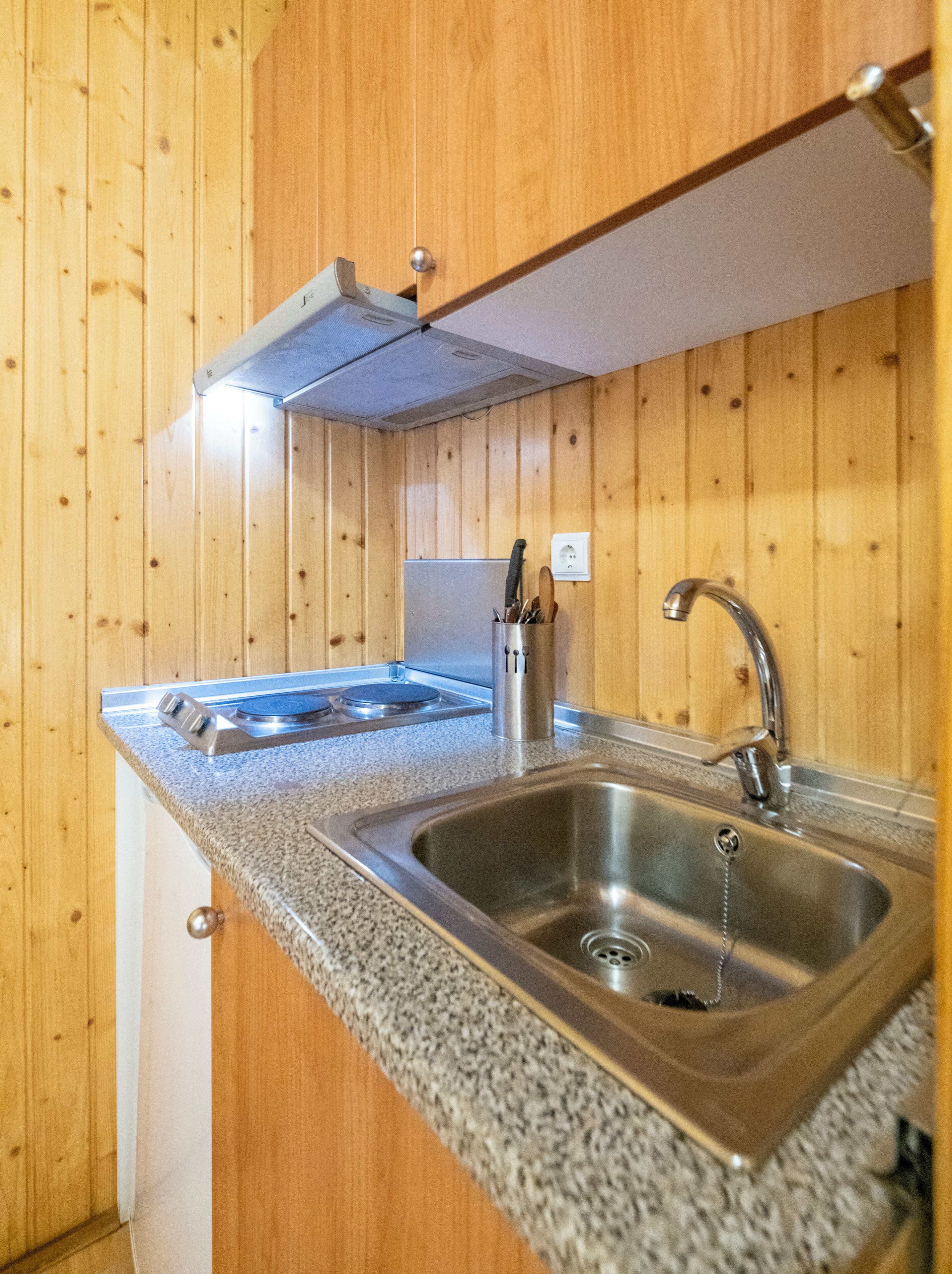 Una cocina con paredes de madera, un lavamanos de acero inoxidable, una estufa y un organizador para cuchillos.