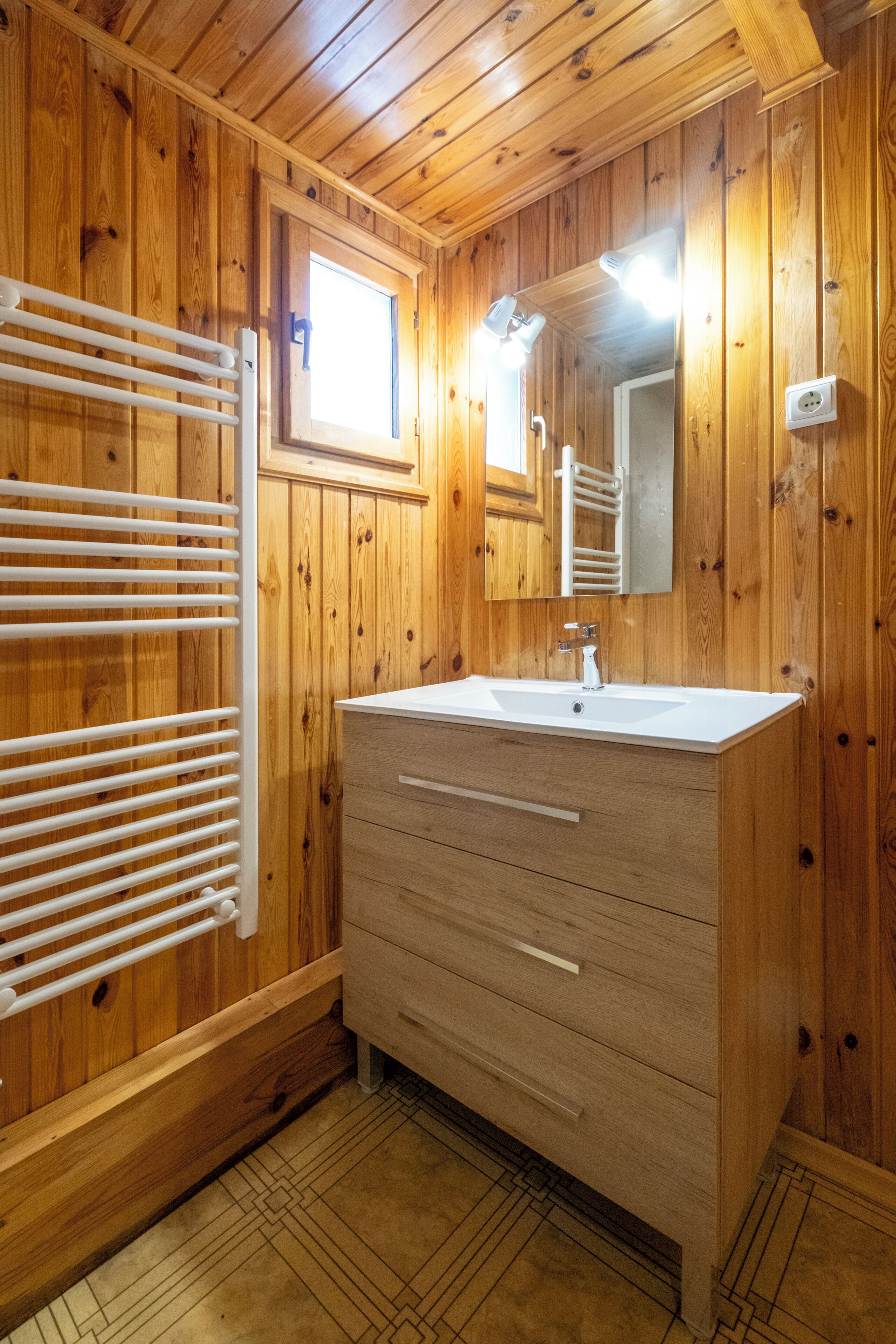 Un baño con paneles de madera, un lavamanos blanco, un espejo y un perchero para toallas.