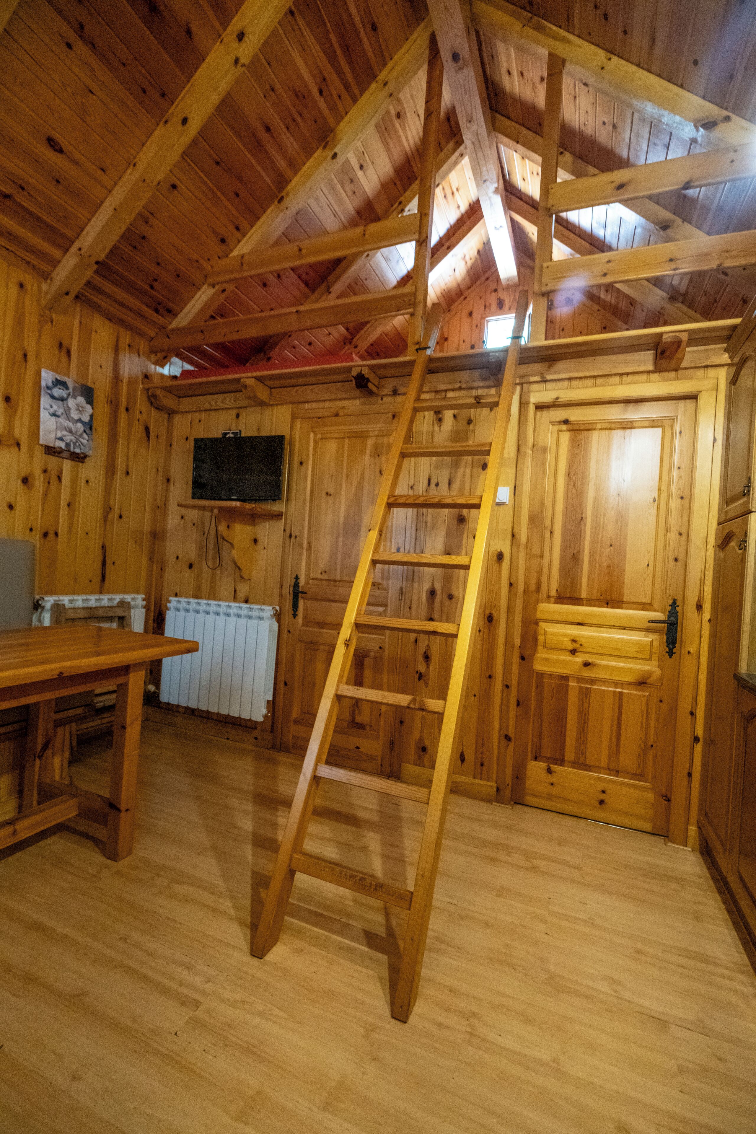 A wooden interior with a wooden ladder, a table, a radiator, and a door.